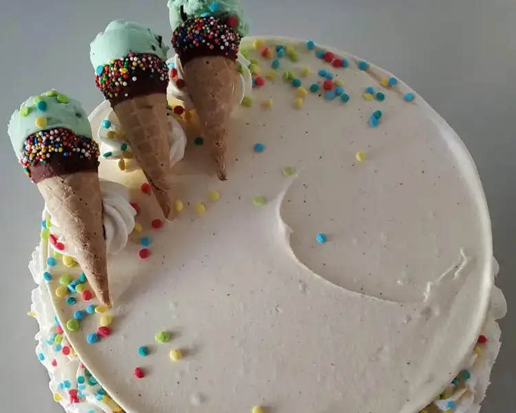 Round ice cream cake with white frosting, three ice cream cones with green ice cream and rainbow sprinkles