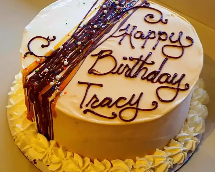 Round cake with light brown frosting, a dark brown stripe, and the words Happy Birthday written in brown icing.