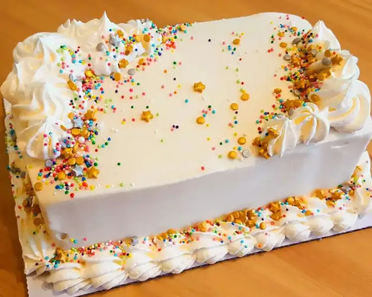 Rectangular cake with white frosting, whipped cream piping, and gold and raibow sprinkles